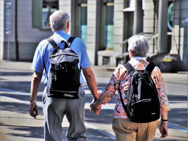 senior couple holding hands with backpacks