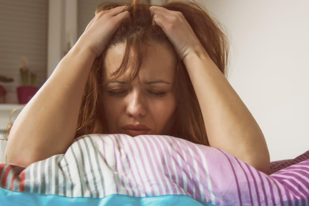 woman over 35 laying in bed with her hands on her head stressed out and so tired.