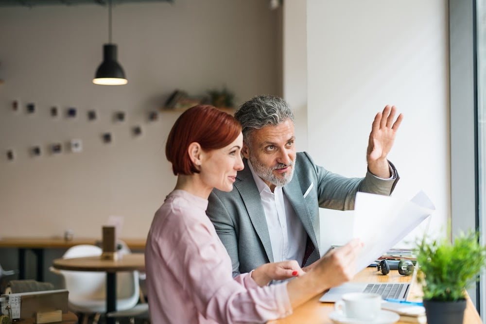 female blogger over 40 with short red hair meeting with an older man who owns a restaurant sitting at a table working on a collaboration to promote your business to the community