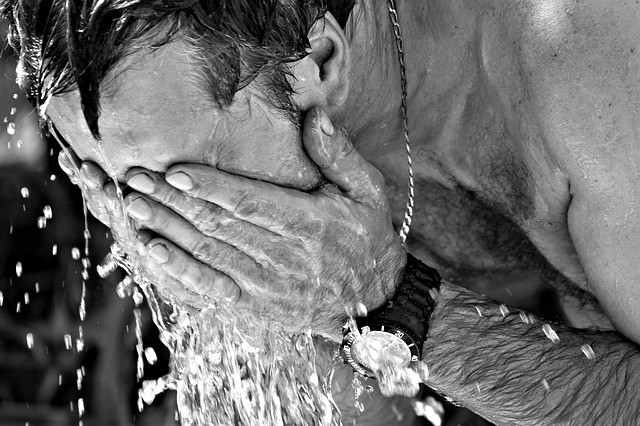 man washing his face in a fountain staying hydrated in the heat