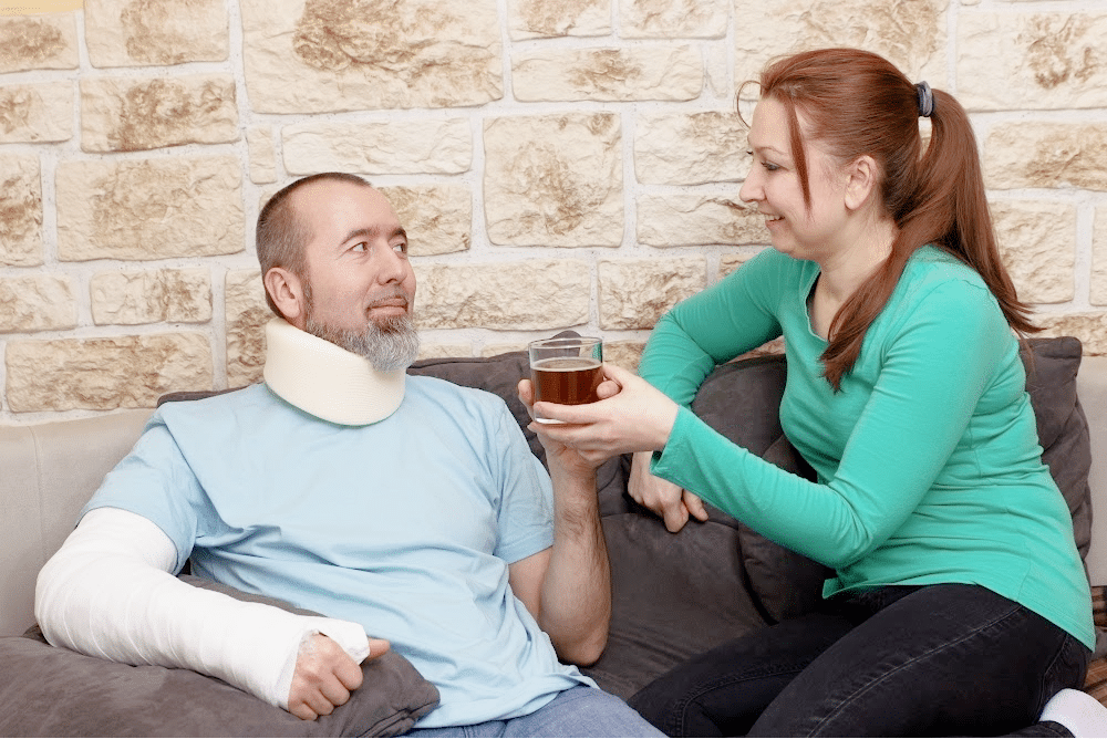 woman with her hair in a ponytail helping out a man wearing a neck brace and his arm in a cast after being injured in a car wreck