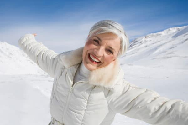 woman over 50 with silver hair in the snow with a white coat smiling reminding you to winterize yourself