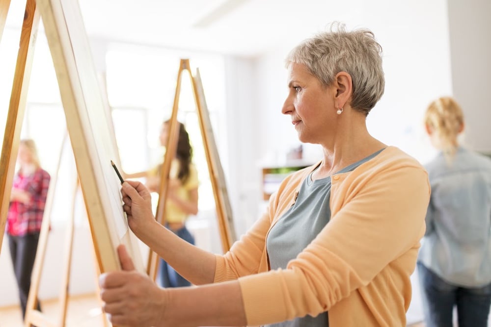 woman over 50 painting and being creative to improve her mental health in a class
