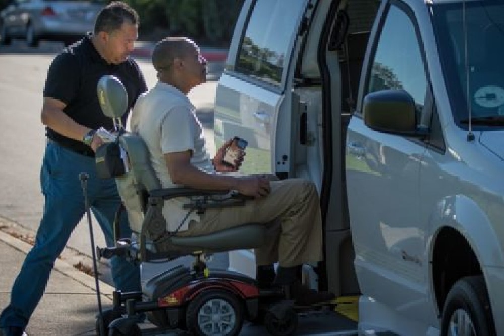 Main helping another man with mobility problems in a wheelchair get into a wheelchair accessible van.