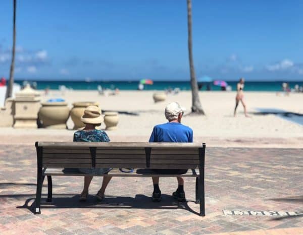retired couple sitting on a bench at the beach