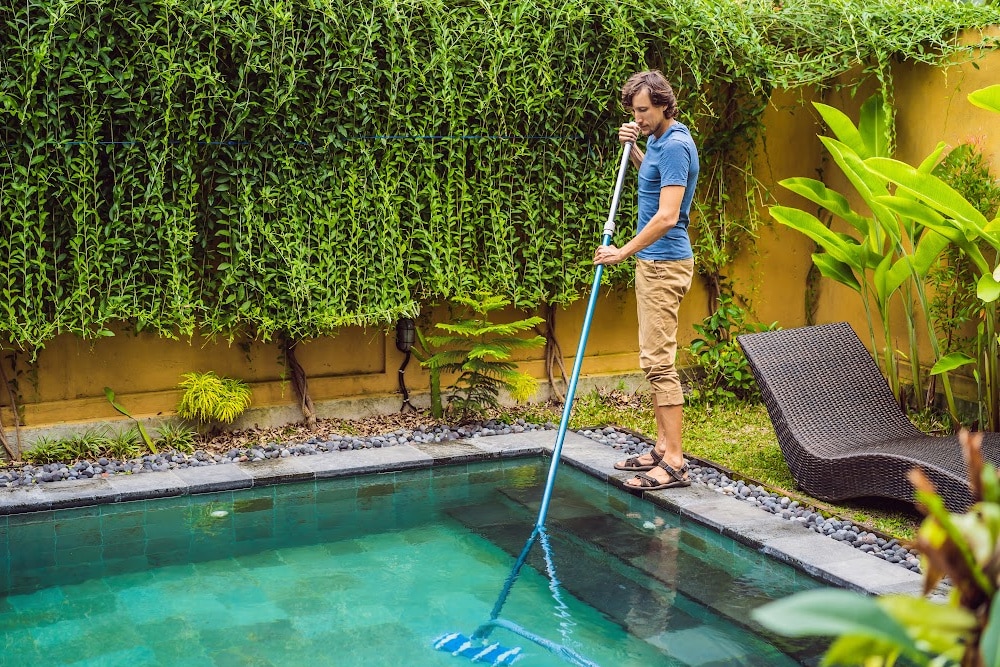 a man cleaning and inground pool with a skimmer