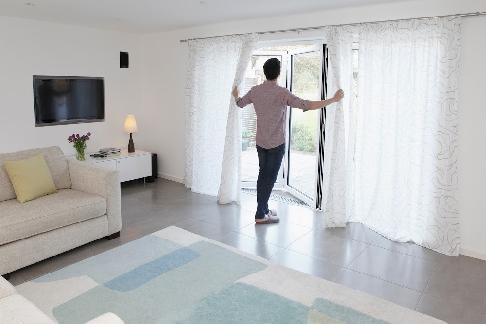 man opening sheer curtains to let light into his summer living room