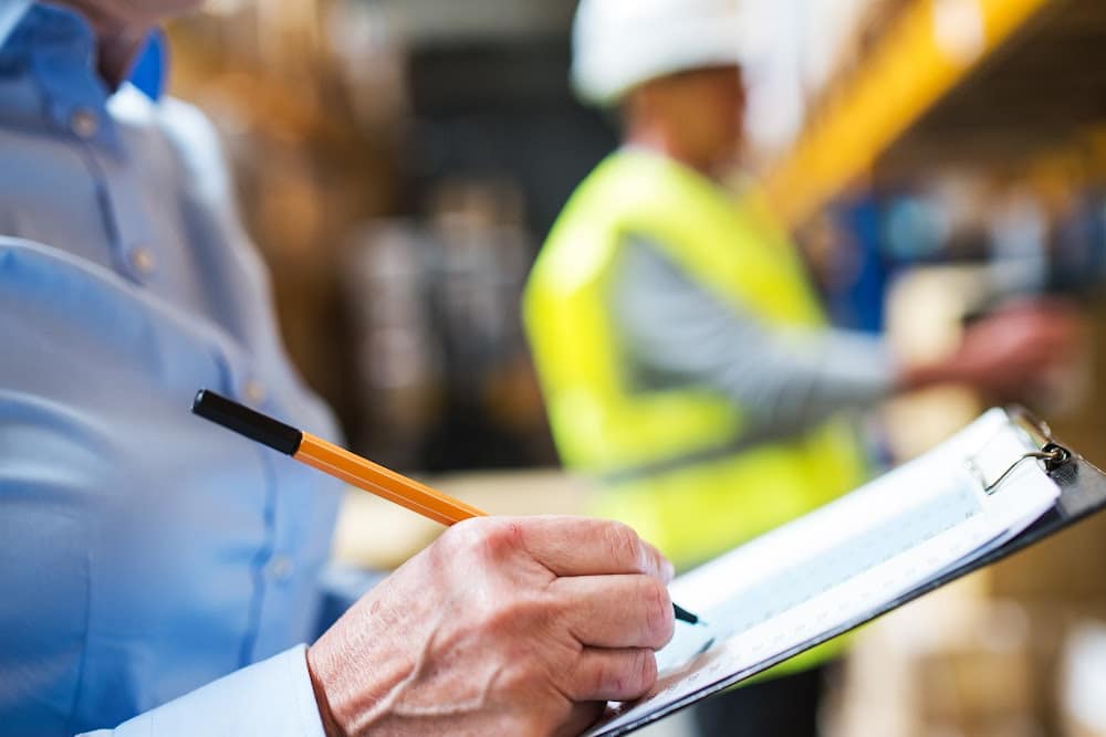 woman over fifty general contractor holding a clipboard with a checklist for materials to renovate and a worker wearing a hard hat.