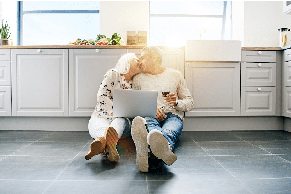 empty nest couple sitting in the kitchen floor planning for retirement on a laptop