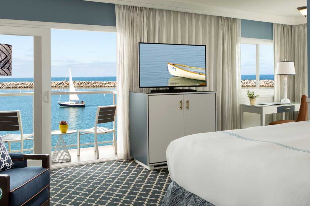 a seaside motel room with nice furnishing and an ocean view patterned carpet and a tv with a boat on it.