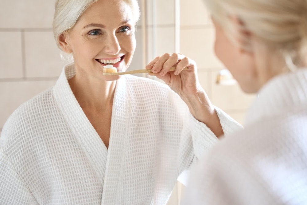 woman over 50 smiling and brushing her teeth