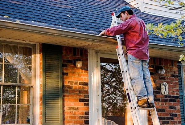 man on a ladder cleaning out roof gutters