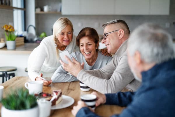 People over 40 laughing sitting around a kitchen table looking at a phone.