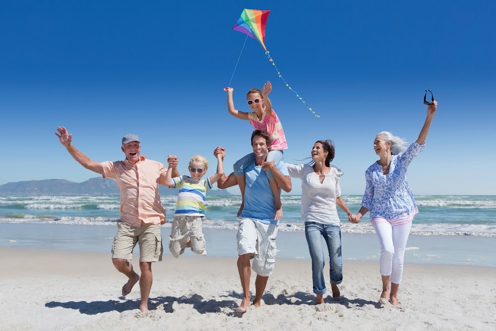 grandparents adult children and grandchildren on the beach with a kite