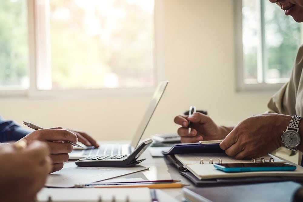 people sitting at a table discussing retirement investments and real estate with papers and a laptop