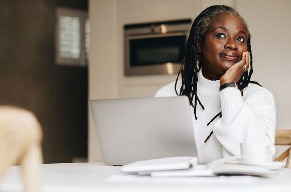 Woman over 50 sitting in front of a laptop thinking about workplace retirement plans.