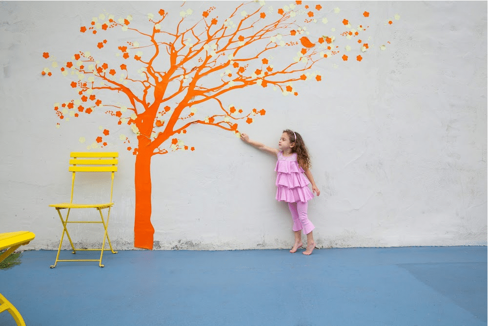 little girl putting up a peel and stick wallpaper tree mural in a playroom