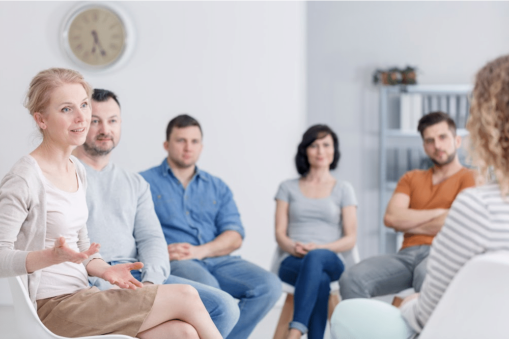 a group of adults in a family therapy session setting in a circle