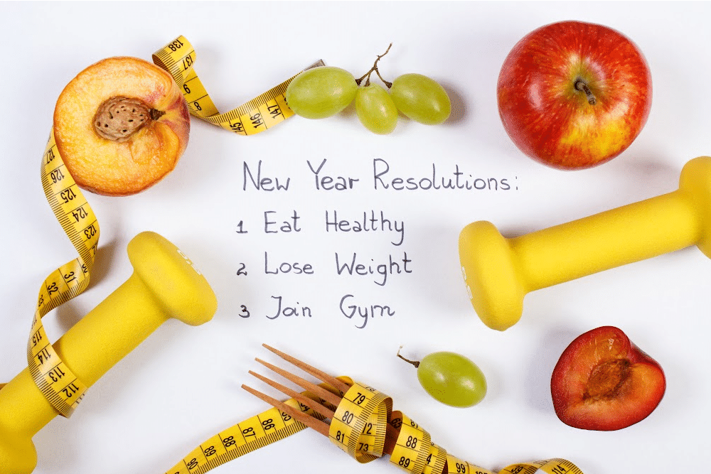 paper with a list of new years resolutions surrounded by vegetable a tape measure, hand weights