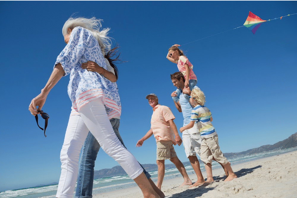 woman over 50 with adult child and grandchildren walking on the beach with men