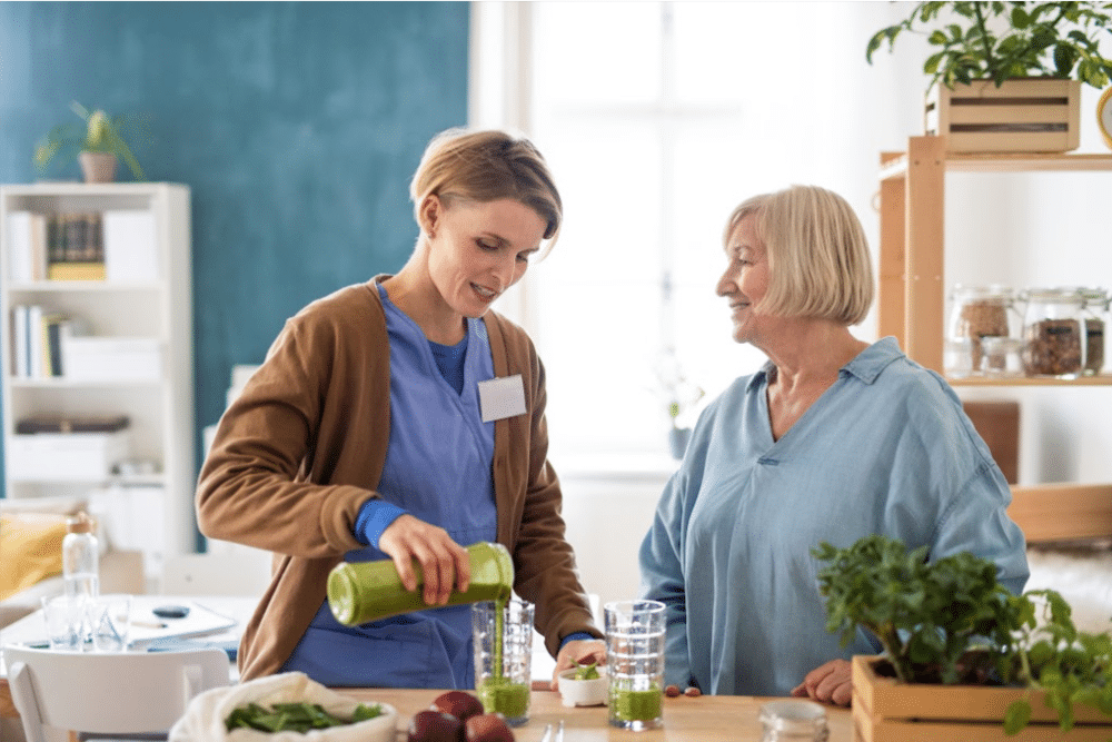 in home health services worker and a woman over 50 in the kitchen making green smothies