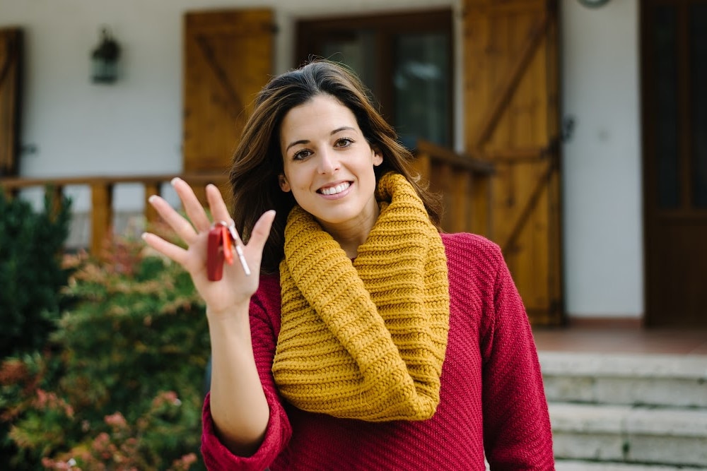 realtor woman over 40 with keys in her hand standing in front of a house smiling