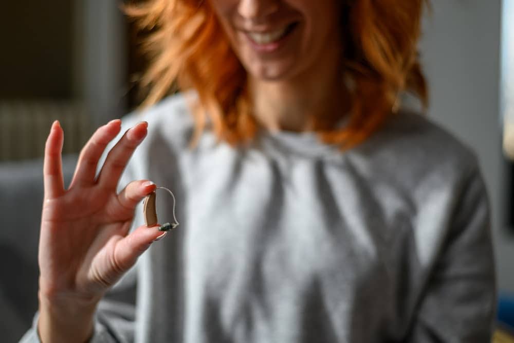 redheaded woman over 40 holding a hearing aid in her hand.
