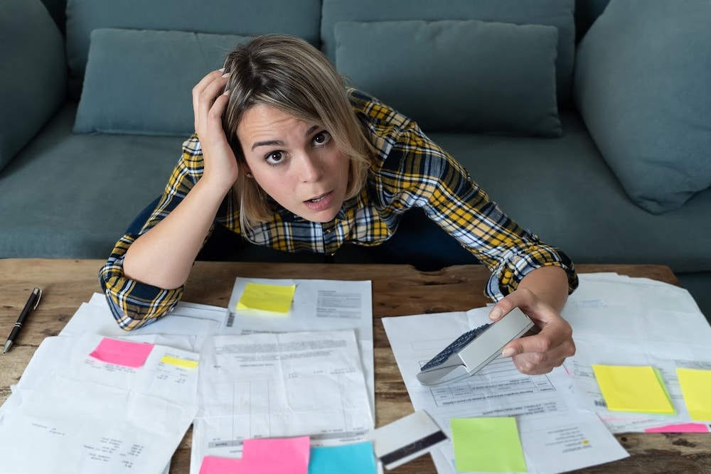woman small business owner trying to fill out tax forms looking very stressed with papers and post it notes spread out on the coffee table in front of her