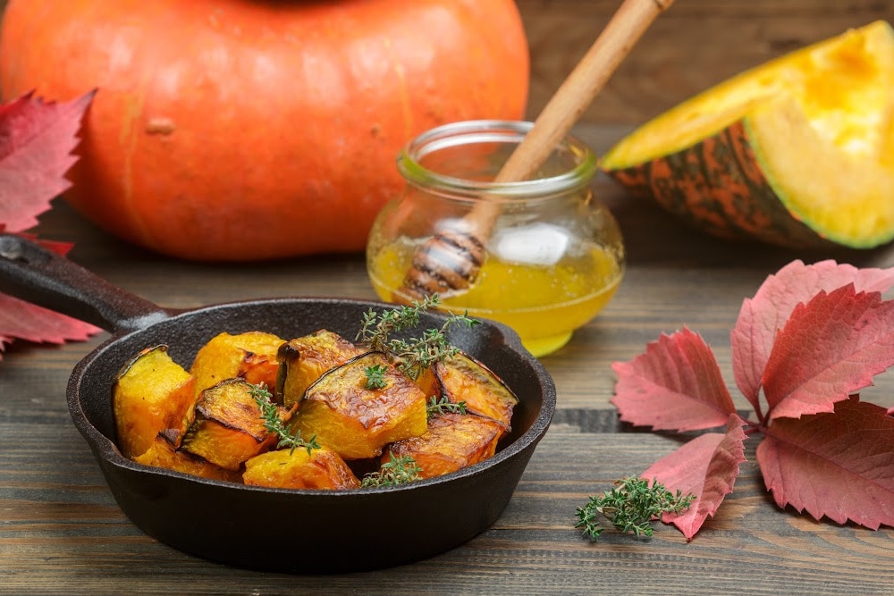 roasted sweet potato pumpkin squash autumn vegetables on a table with honey in a jar