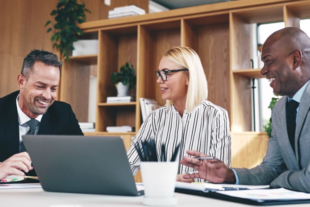 accountants 2 men over 30 and a woman over 40 sitting at a table with a laptop and a cup full of ink pens