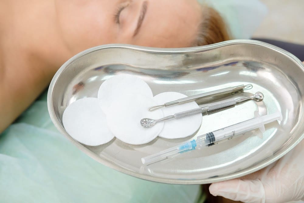 sterile instruments for botox and fillers in a tray with a woman over 40 in the background on an examination table