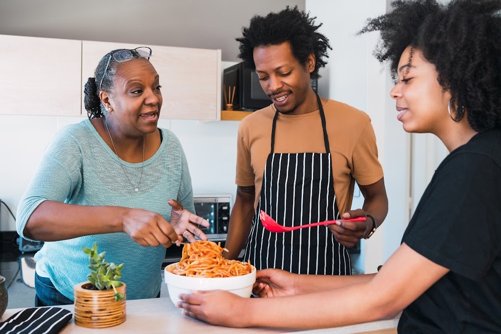 woman over 50 showing her son in law how to make spaghetti while her adult child watches