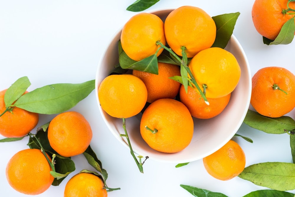 Fresh oranges in a bowl with green leaves