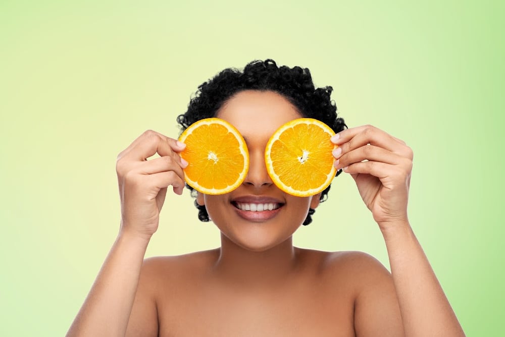 a woman holding orange slices over her eyes