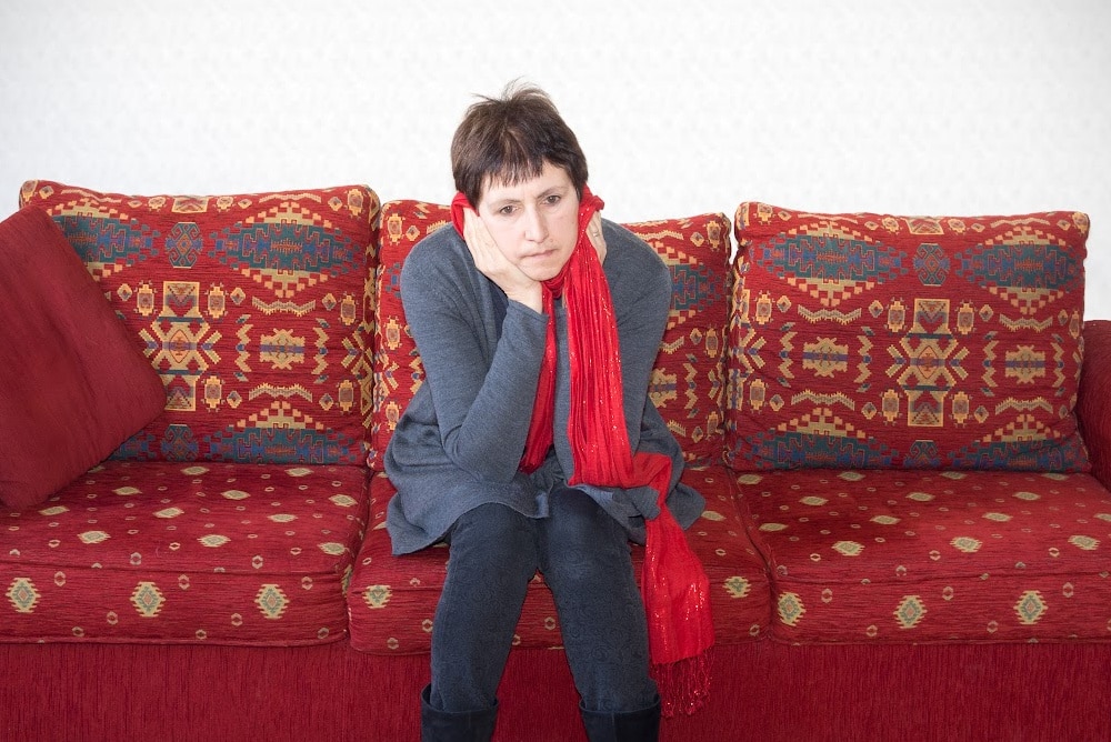 woman over 50 sitting on a read sofa looking depressed