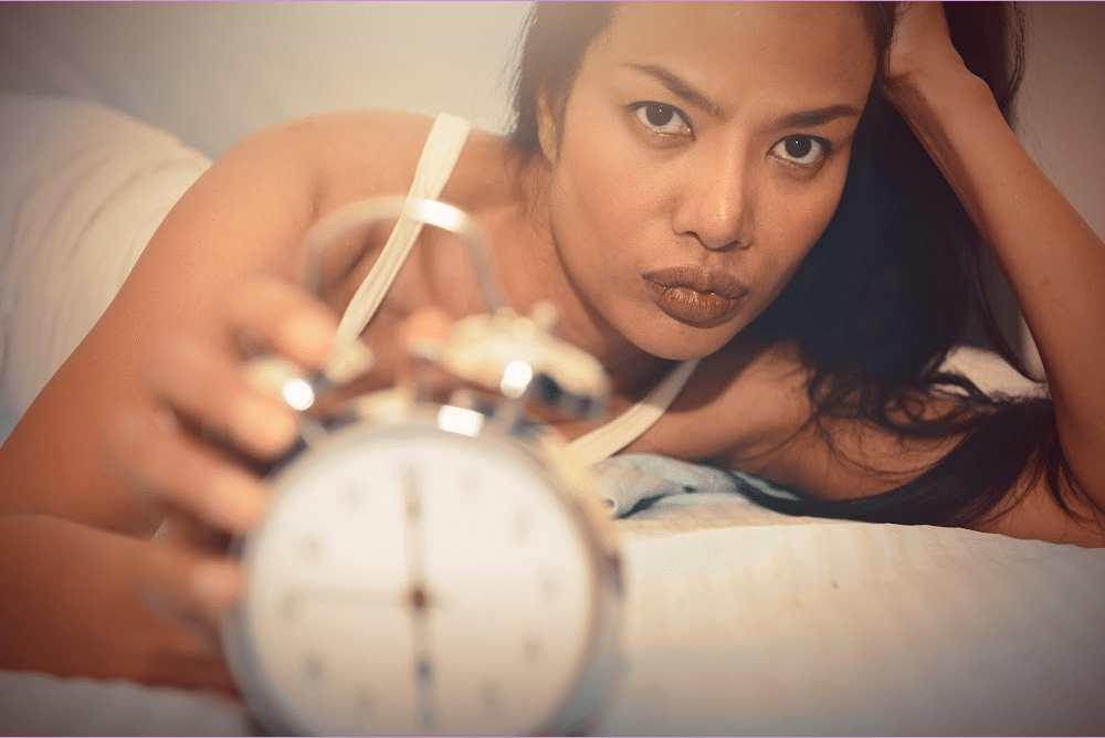woman over 40 with insomnia from menopause with an alarm clock looking angry