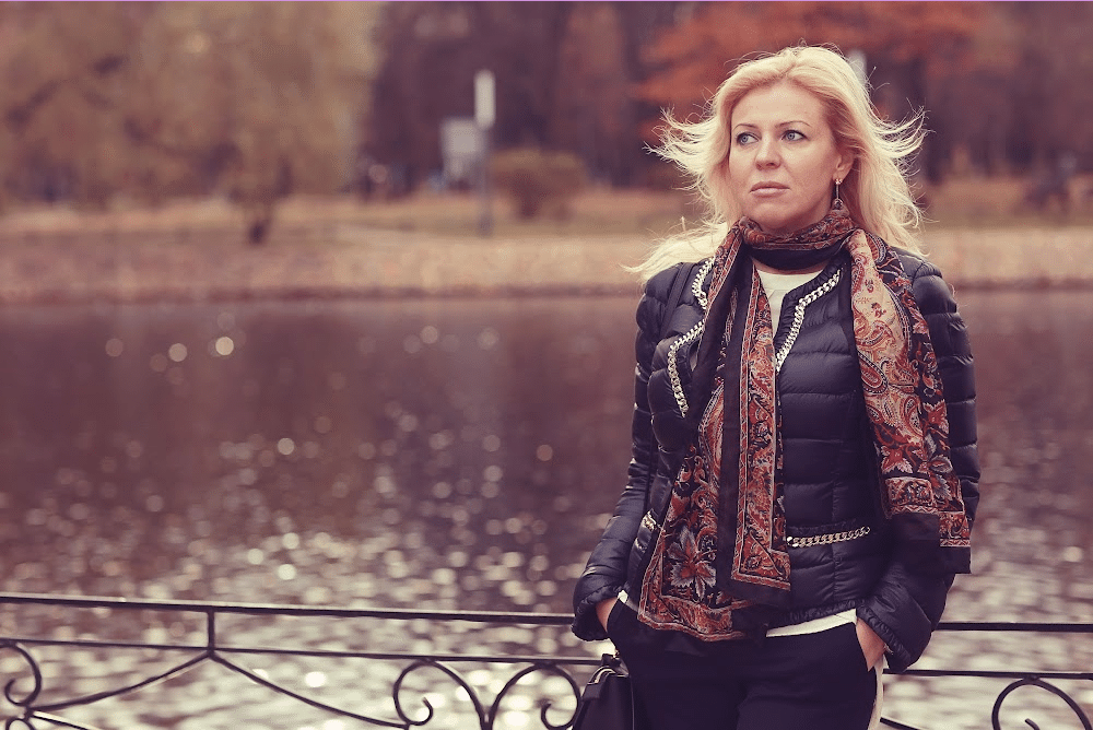 generation x woman over 40 standing near a lake wearing a leather jacket and a scarf