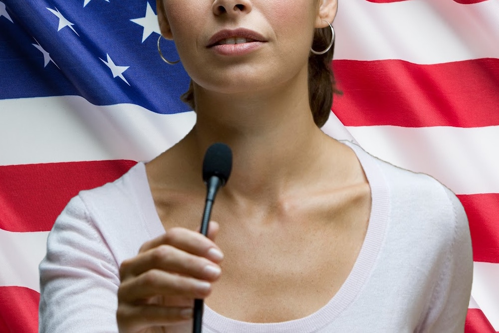 woman speaking into a microphone in front of an american flag