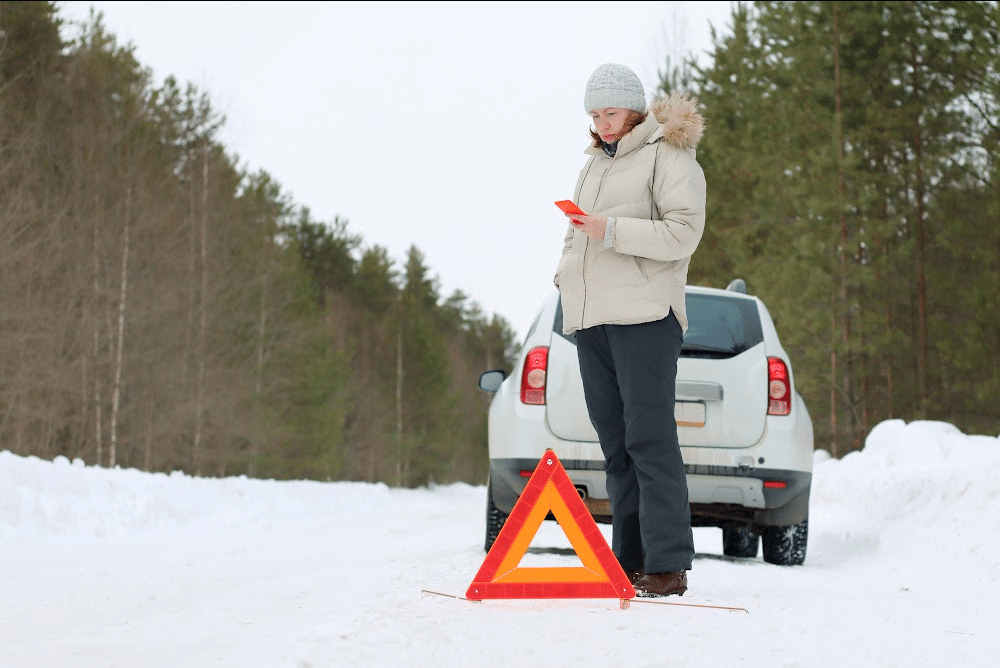 woman using her cell phone in the snow with a car stranded