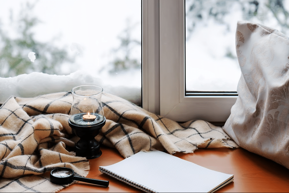 looking out a snowy window with a cozy blanket, journal, and pillow