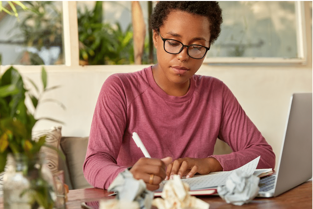 woman sitting at a table rewriting a blog post with balled up paper and a notebook and pen.