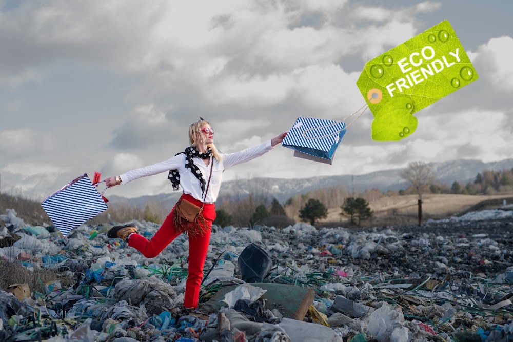 woman with shopping bags standing in a landfill of trash and a tag that says eco friendly